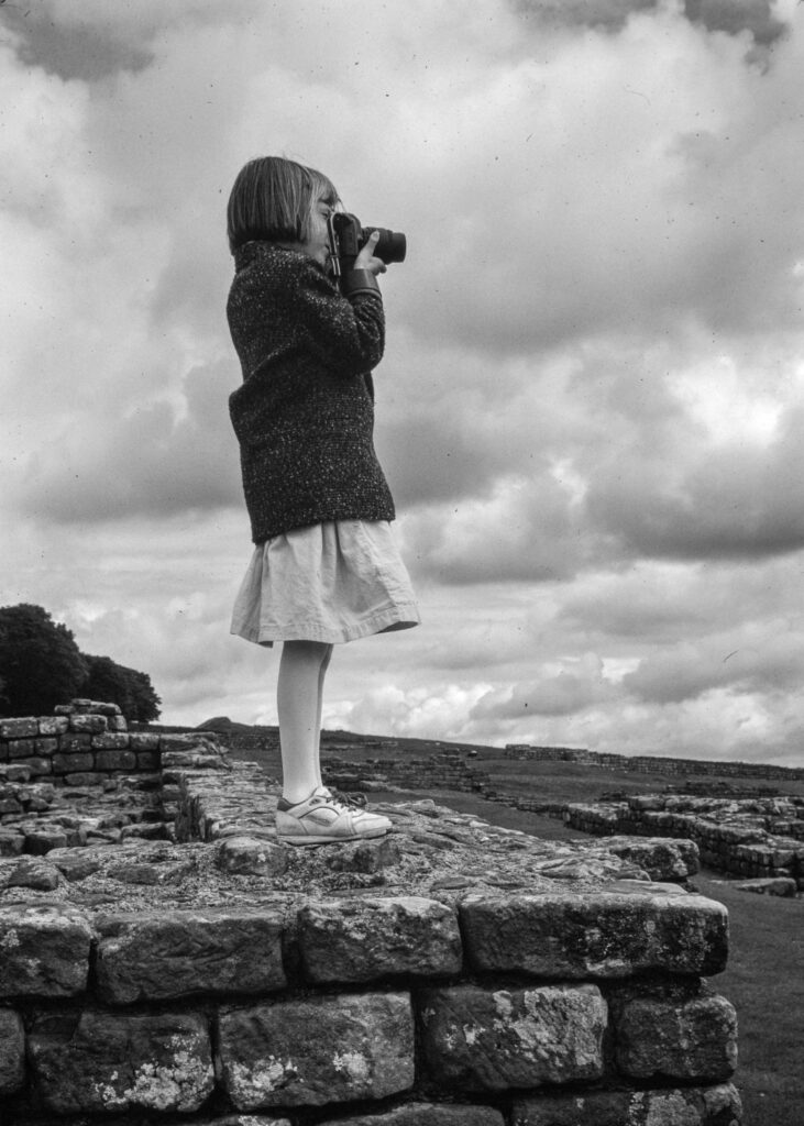 girl standing on Hadrians Wall taking a photo